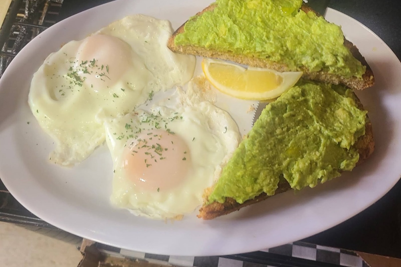 Avocado toast on 9-grain bread with two basted eggs and a lemon wedge